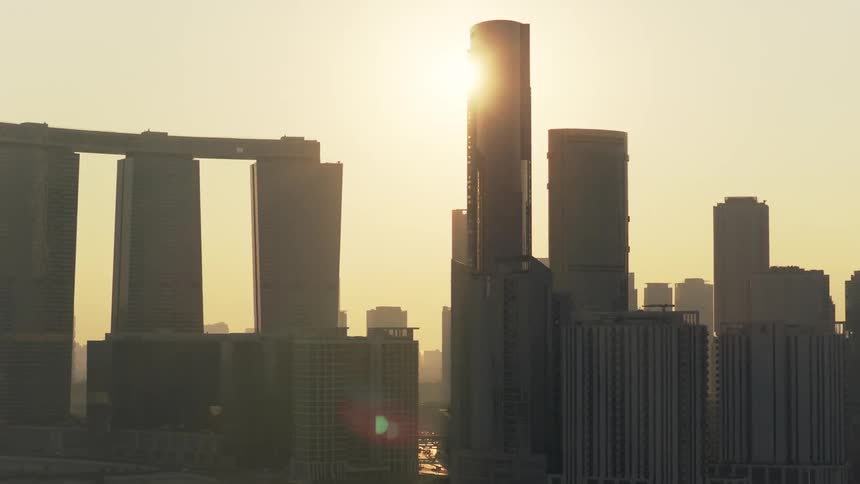 An aerial pullback shot reveals the modern skyline of Abu Dhabi, with iconic skyscrapers silhouetted against a hazy golden sunrise