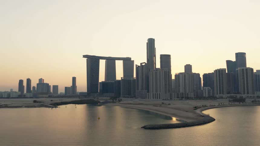 A tranquil aerial view captures the modern Abu Dhabi skyline and its iconic Gate Towers rising over the calm coastline at sunrise