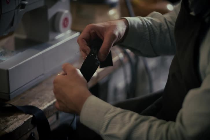 A skilled craftsman carefully hand-stitches a branded label onto a piece of fabric in a workshop