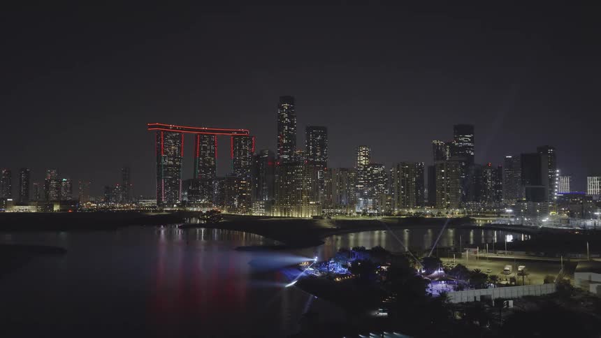 A dazzling nighttime cityscape of Abu Dhabi's Al Reem Island, featuring illuminated skyscrapers and a brilliant light show across the water