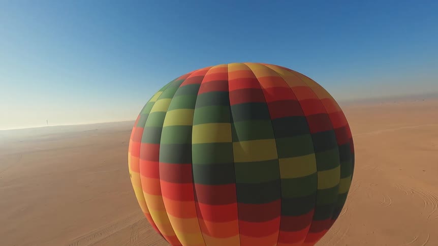 An aerial view of a colorful hot air balloon ascending over the vast desert on a clear, sunny day