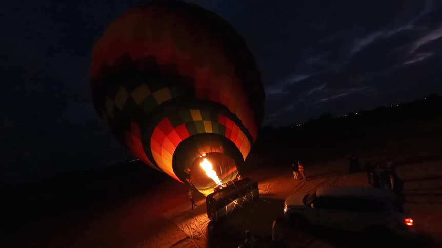 A colorful hot air balloon is inflated with a powerful flame from a burner during the night, preparing for takeoff