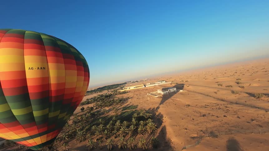 A colorful hot air balloon glides over the vast Dubai desert and a lush oasis on a clear day