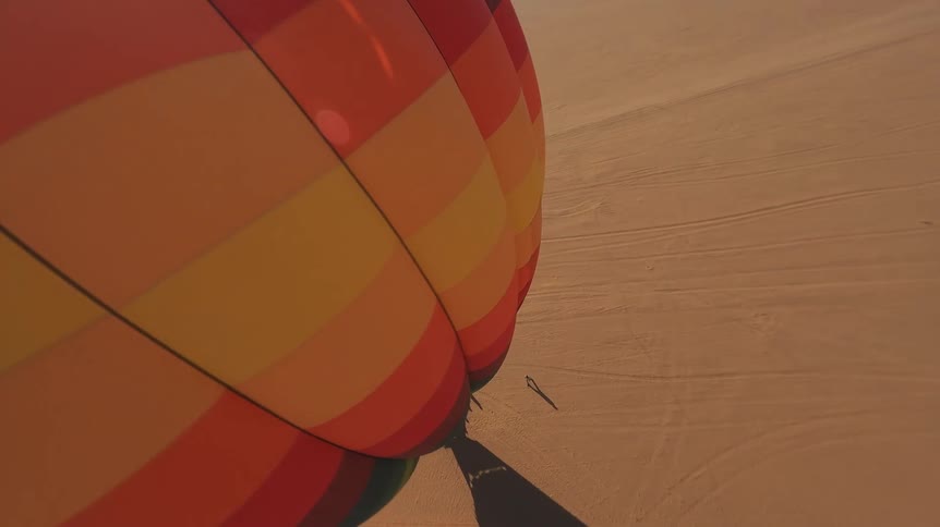 A POV from a colorful hot air balloon as it soars over a vast desert and then gracefully lands on the sand