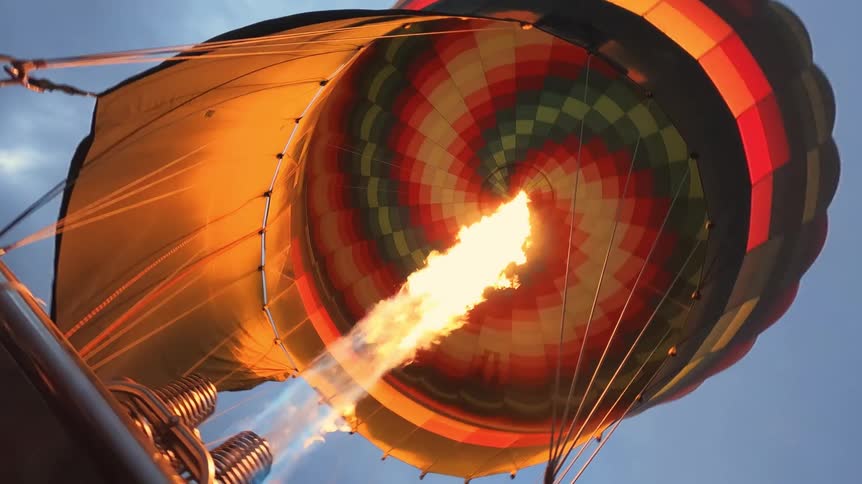 A powerful flame from a burner inflates a colorful hot air balloon in slow motion, shot from a low angle