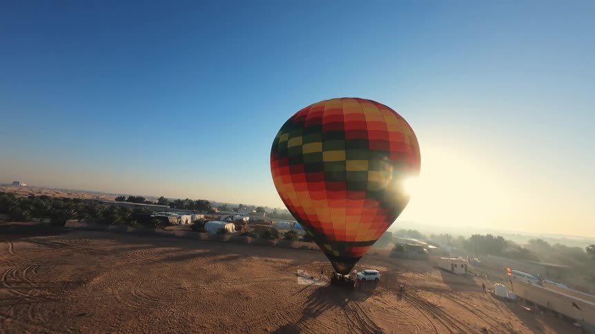 An aerial view shows a colorful hot air balloon on the ground in the desert as the sun rises in a brilliant flare