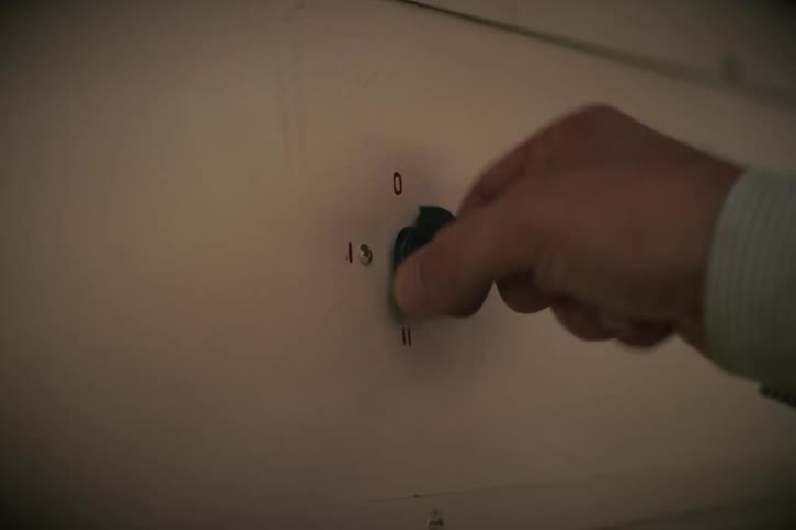 A close-up shot shows a hand turning a mysterious black dial on a white panel up to the number eleven