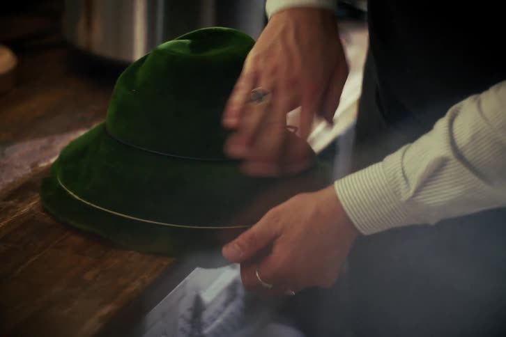 A skilled hatter's hands meticulously put the finishing touches on a traditional green velvet hat in a workshop