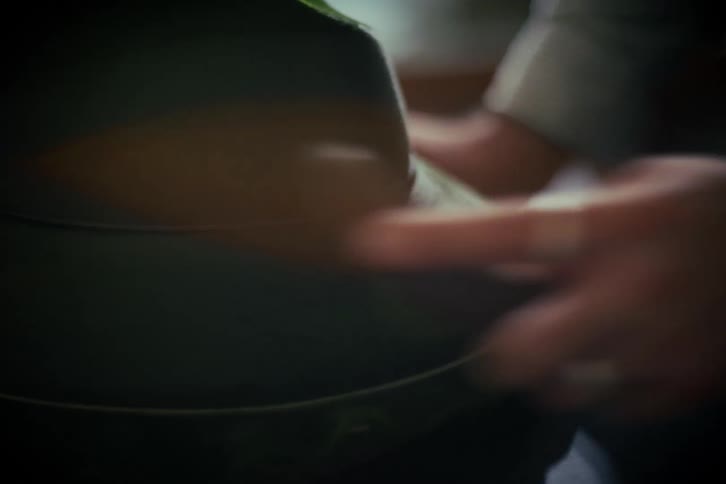 A close-up shot of a person's hands meticulously cleaning and brushing a classic green felt hat