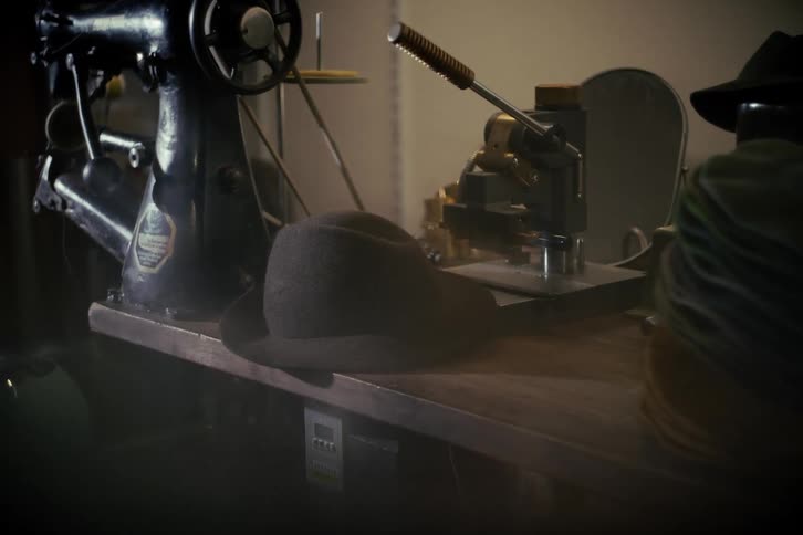 Atmospheric still shot of a vintage hat maker's workshop with a fedora and old machinery on a desk