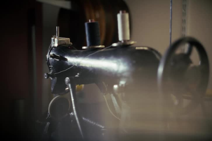 A moody close-up of a classic black sewing machine with thread spools sitting idle in a hazy workshop