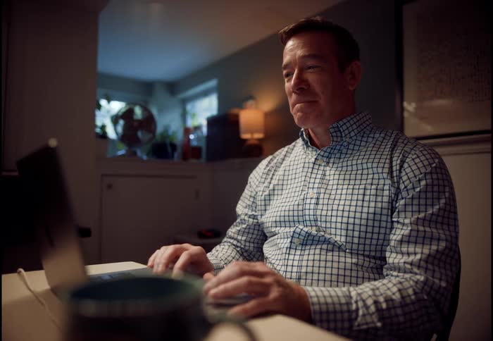 A man's demeanor shifts from cheerful to stressed while on a video call on his laptop in a dimly lit home office
