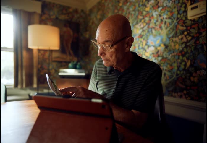 An elderly man with glasses enjoys a video call on his tablet while sitting at a table in his cozy home