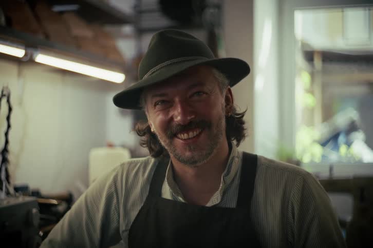 Close-up portrait of a friendly artisan with a mustache and hat smiling in his workshop