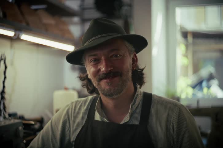 Portrait of a proud, smiling artisan with a mustache wearing a traditional hat and apron in his workshop