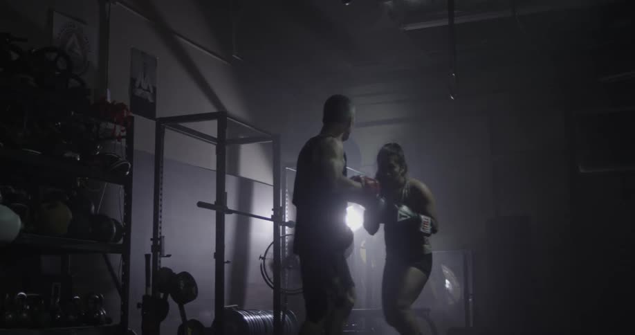 Woman boxing with a trainer in a dark area