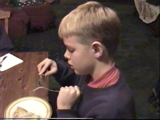 Vintage home video footage of two young boys eating dessert at a table with a Christmas tree in the background