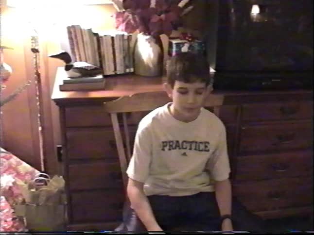 Boy in a party hat sits in a bedroom opening a gift in warm home video footage