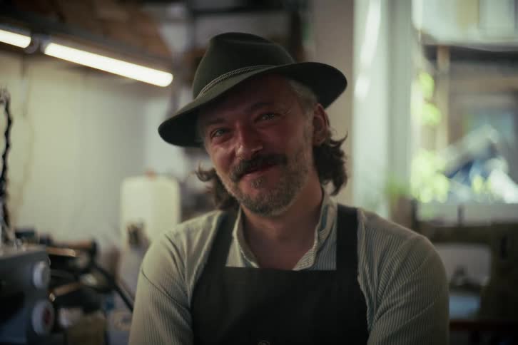 Portrait of a charming male artisan with a mustache and traditional hat smiling kindly in his workshop