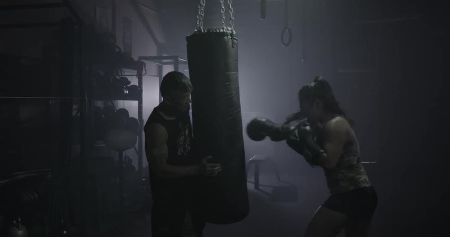 Man holds a punching bag while a woman punches it