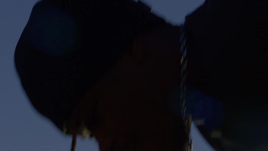 A mysterious person in a dark hoodie is silhouetted against a deep blue sky in this moody, low-angle close-up