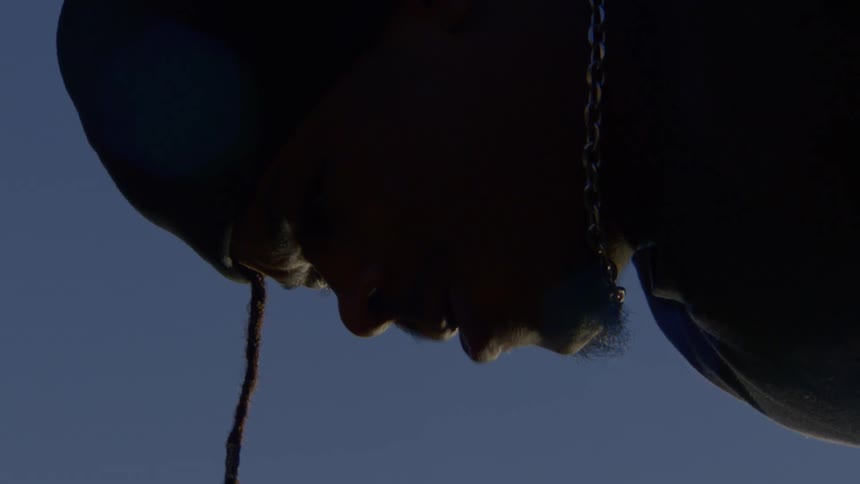 Dramatic low-angle slow motion shot of a young man's silhouetted face against the clear blue sky