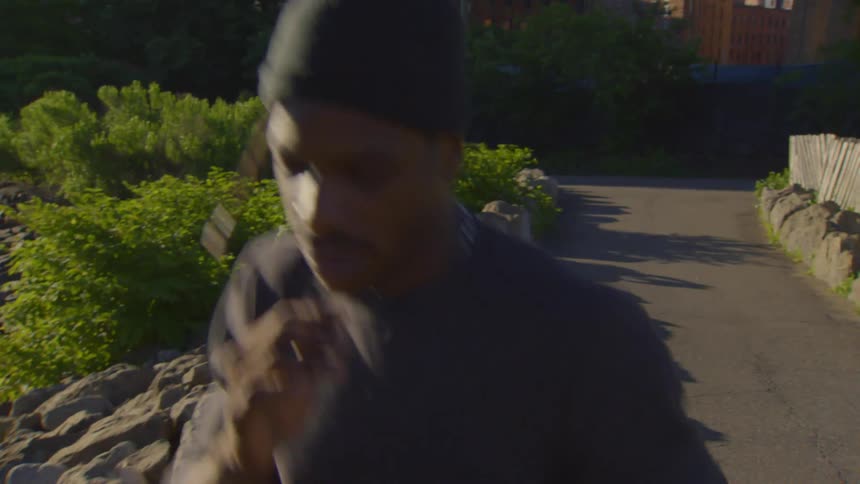 A focused man shadowboxes while jogging along a sunlit pathway in a city park during golden hour