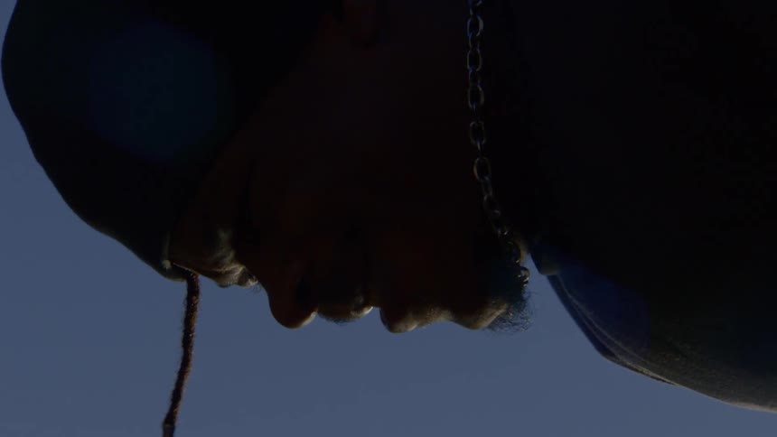 Low-angle close-up of a silhouetted man with his head bowed in contemplation against a clear blue sky