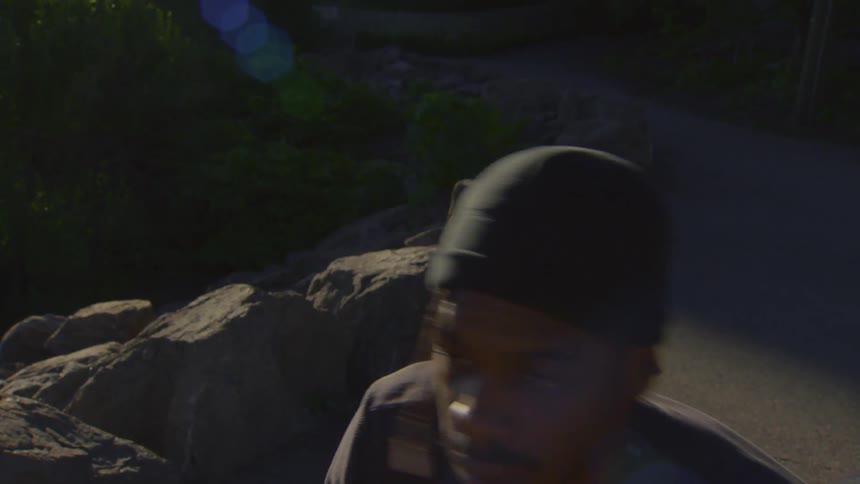 A focused young man wearing a beanie intensely shadowboxes in a sunlit outdoor park