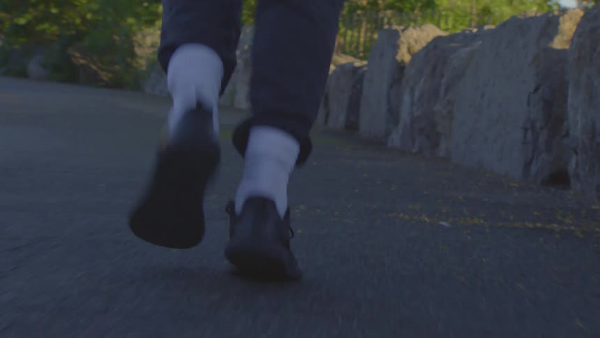 Low angle close up of a person's feet walking along a paved path in a park at sunset