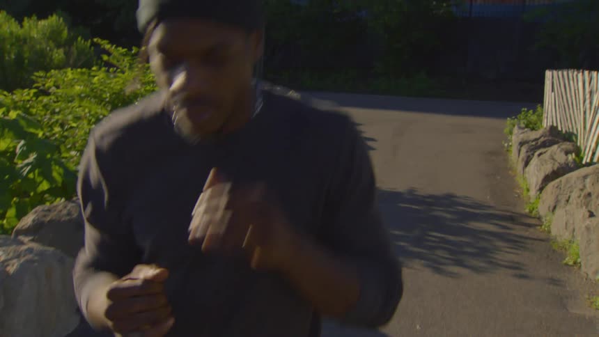 An athletic young man jogs in place and shadowboxes while warming up in a city park at golden hour