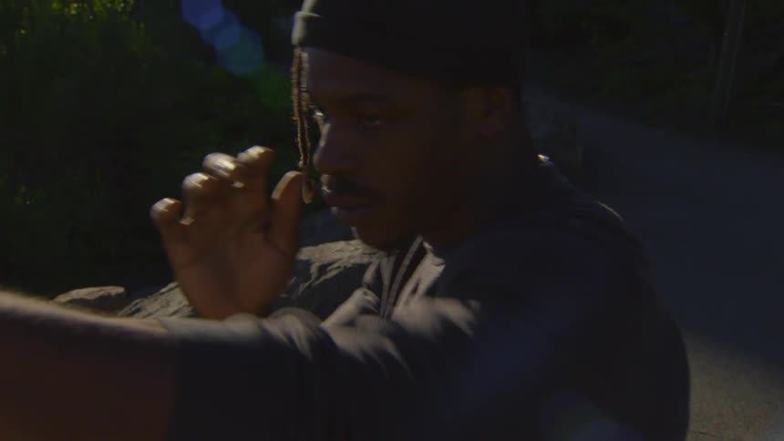 A determined young man in a beanie performs a slow, focused martial arts routine outdoors among rocks and trees
