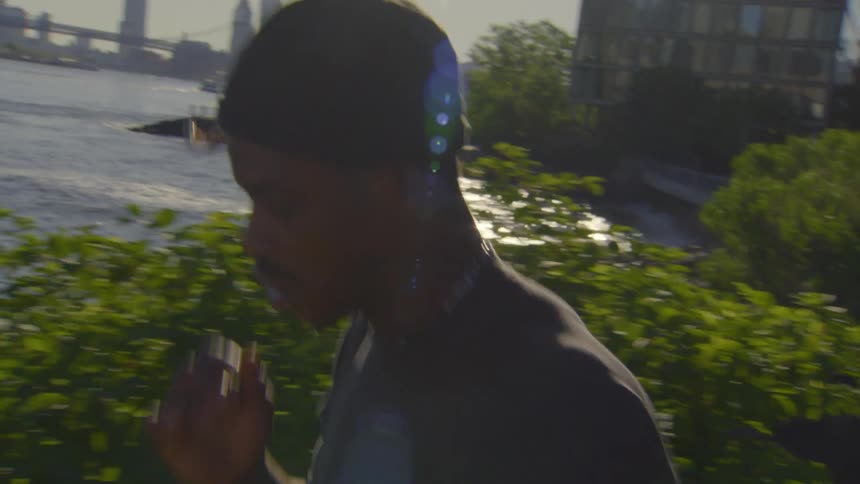 A young man grooves along a sunny, urban waterfront, dancing with passion as the city skyline looms in the background