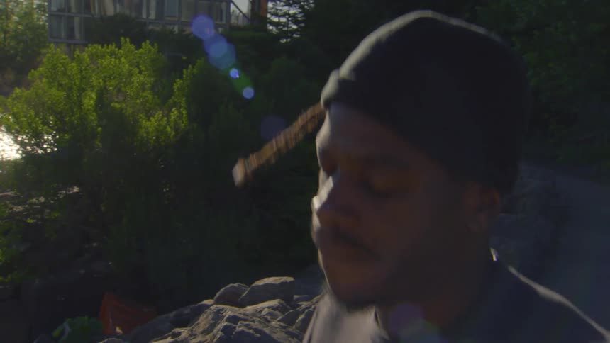 A young man wearing a beanie jogs in place in slow motion, with the bright sun creating a lens flare behind him