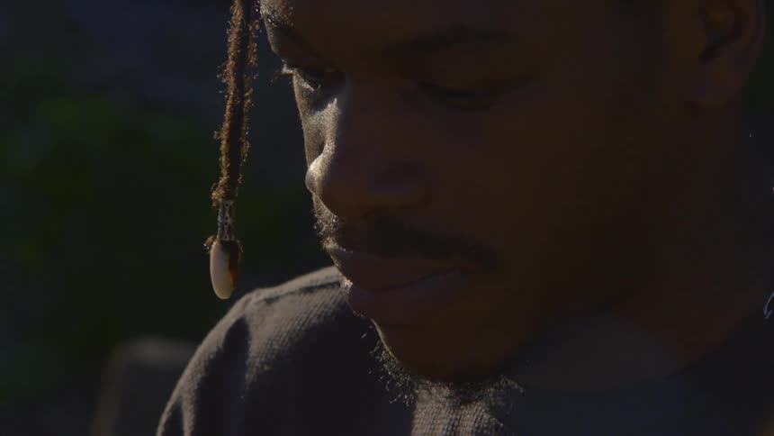 A slow-motion, intimate close-up captures the pensive expression of a young Black man in dramatic lighting