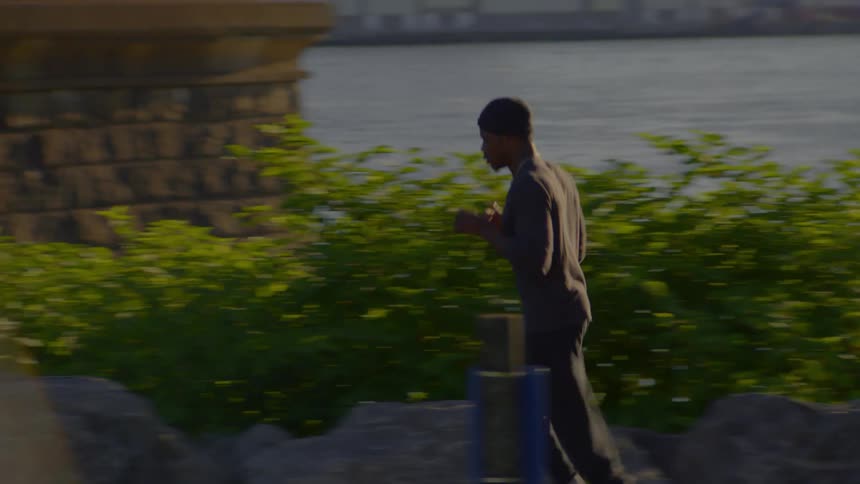 Slow motion side view of a man jogging along a rocky path next to a river during sunset
