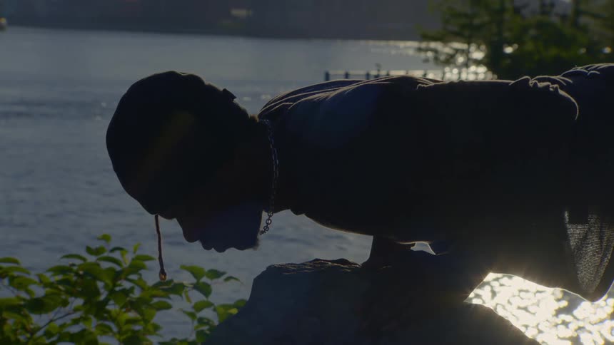 A man in silhouette holds a plank position on a rock while exercising by the water at sunrise
