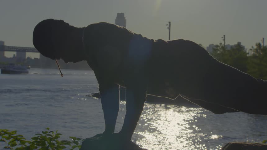 A person holds a difficult yoga pose in silhouette as the sun rises over the river and New York City skyline