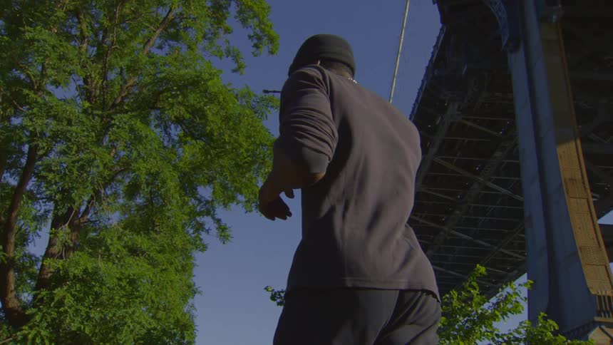 Looking up from a low angle at a man standing still under a large bridge next to lush green trees