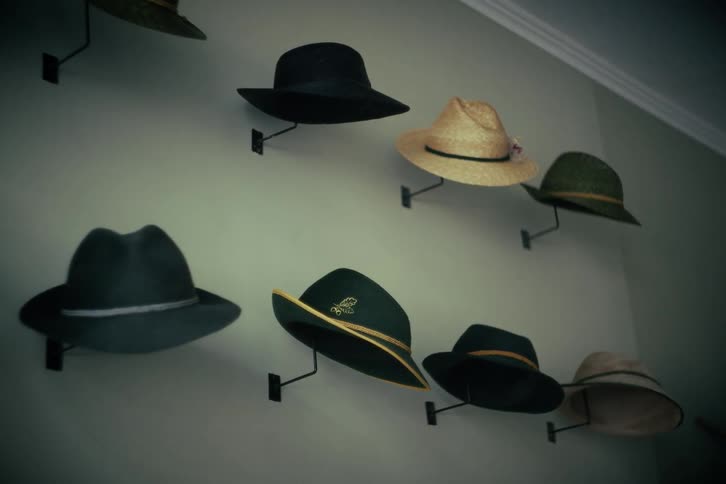 A collection of various classic and vintage style hats are mounted and displayed on a light-colored wall