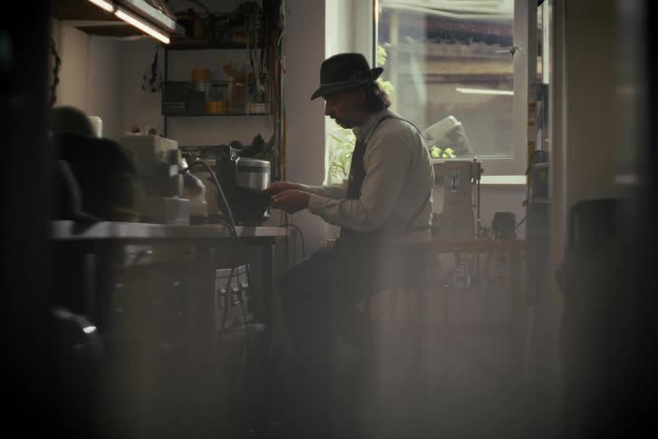 A skilled hatter meticulously crafts a felt hat in his traditional, dimly lit workshop