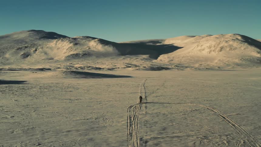 Aerial view of a lone cyclist riding a fat bike through a vast, snow-covered arctic landscape at sunrise