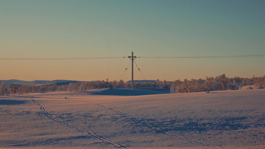 A solitary power pole stands in a vast snowy landscape illuminated by the warm light of a winter sunrise