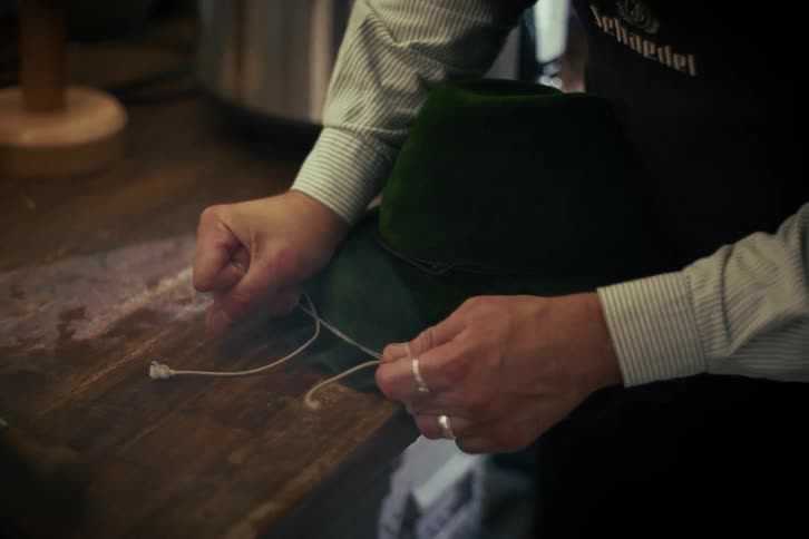 A craftsman carefully ties a decorative cord around the crown of a traditional green felt hat in his workshop