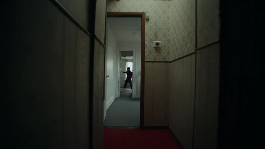A slow push-in shot down a dark, creepy hallway reveals a masked dancer performing in an empty, dilapidated room