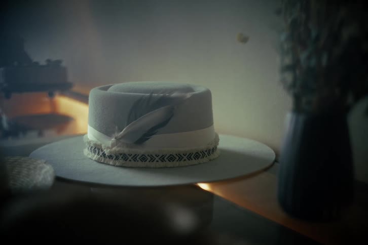 Cinemagraph loop of a stylish bohemian hat with a decorative feather resting on a table in a dimly lit room
