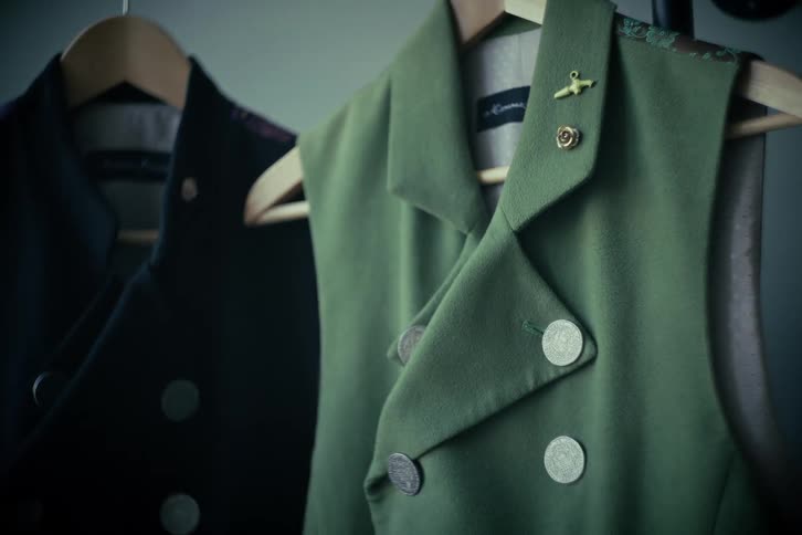 A close-up of a stylish, olive green, military-inspired vest with coin buttons and an airplane pin hanging in a clothing boutique
