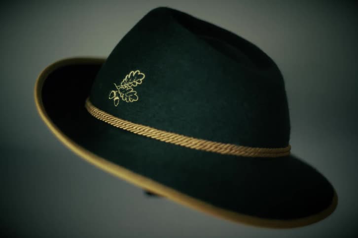 A classic green felt Tyrolean hat with an embroidered oak leaf and acorn emblem is shown in a studio setting