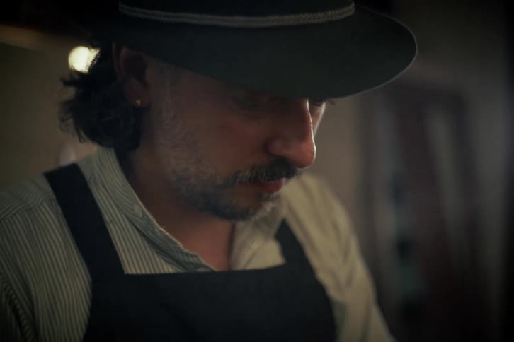 Close-up of a focused hatter meticulously hand-stitching the finishing touches on a traditional felt hat in his workshop