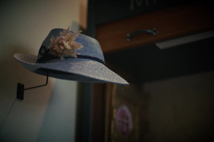 A stylish blue ladies' hat with a feather hangs on a hook in a dimly lit, moody interior